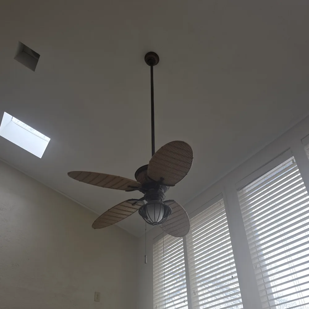 A ceiling fan hung on a downrod from a vaulted ceiling beside a skylight