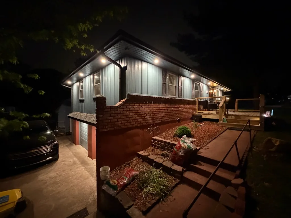 A ranch house at dusk with soffit downlighting along the eaves and uplighting in the beds below
