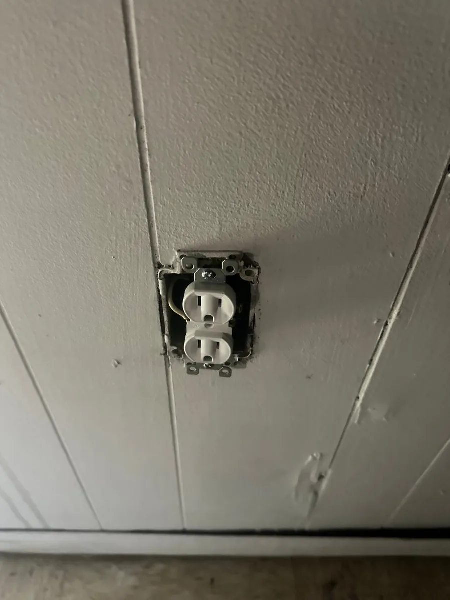 An old receptacle hanging loose from its box in a painted wall