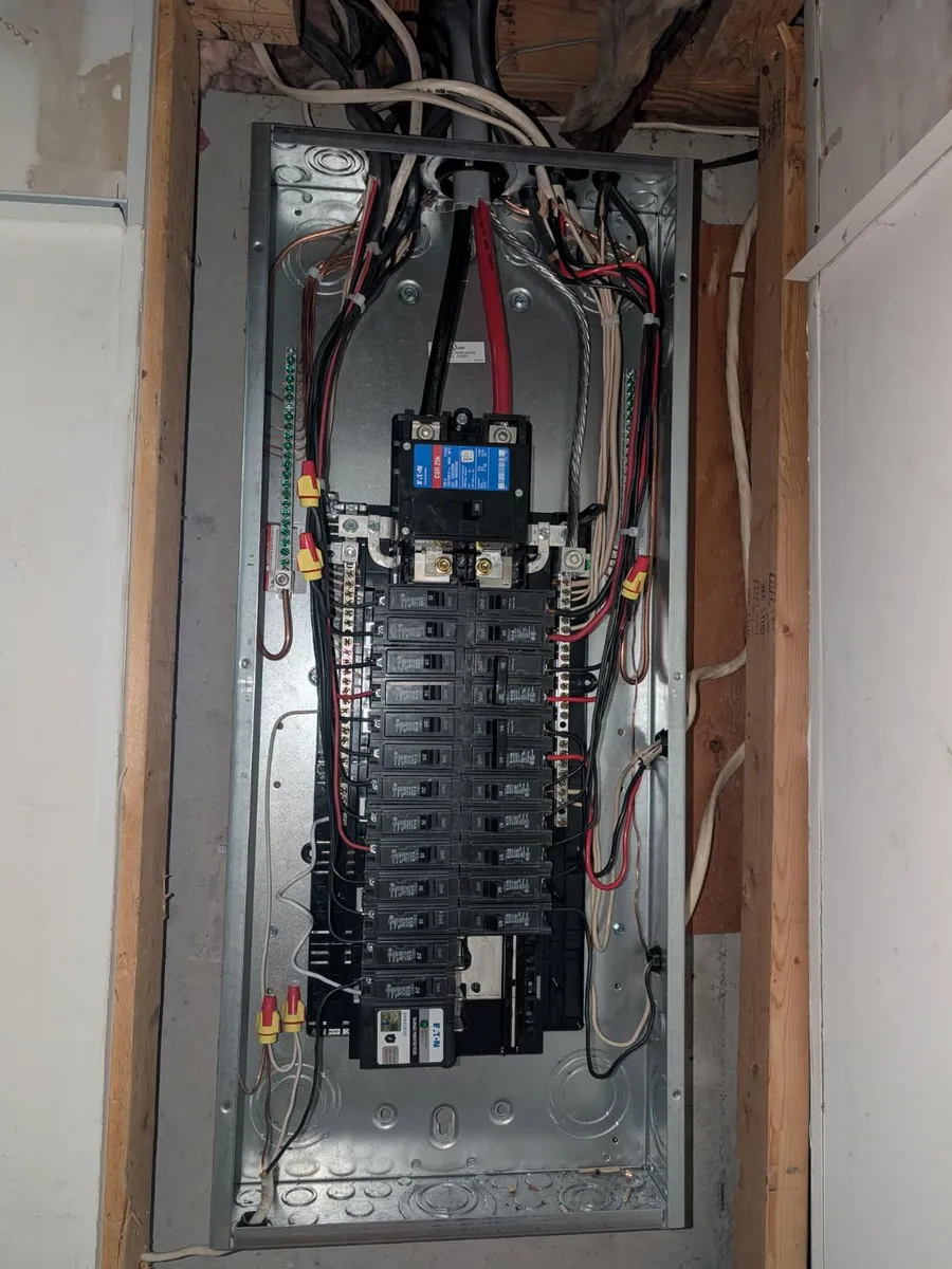A new Eaton panel set into a framed wall with the breakers landed and the cover still off