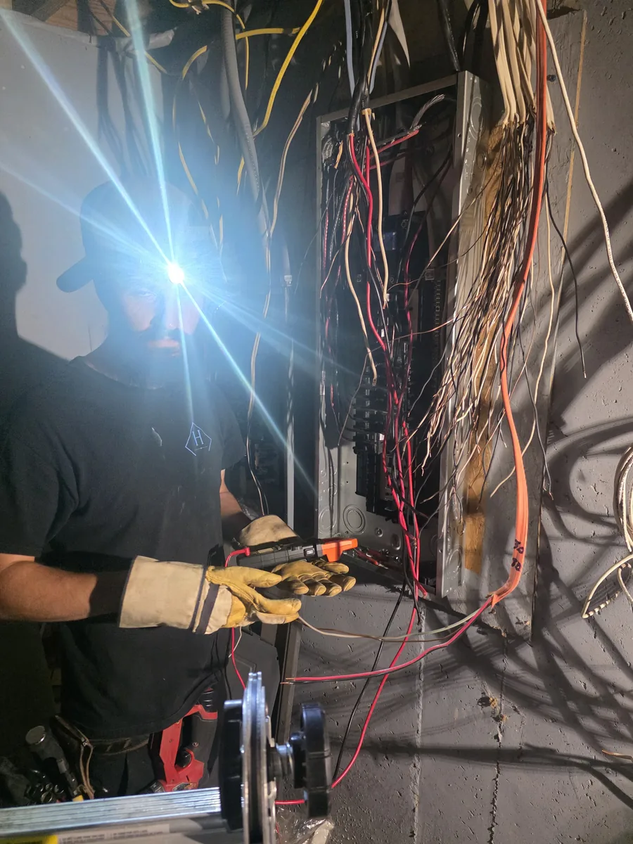 An electrician working inside an energised panel with the cover off, testing a circuit