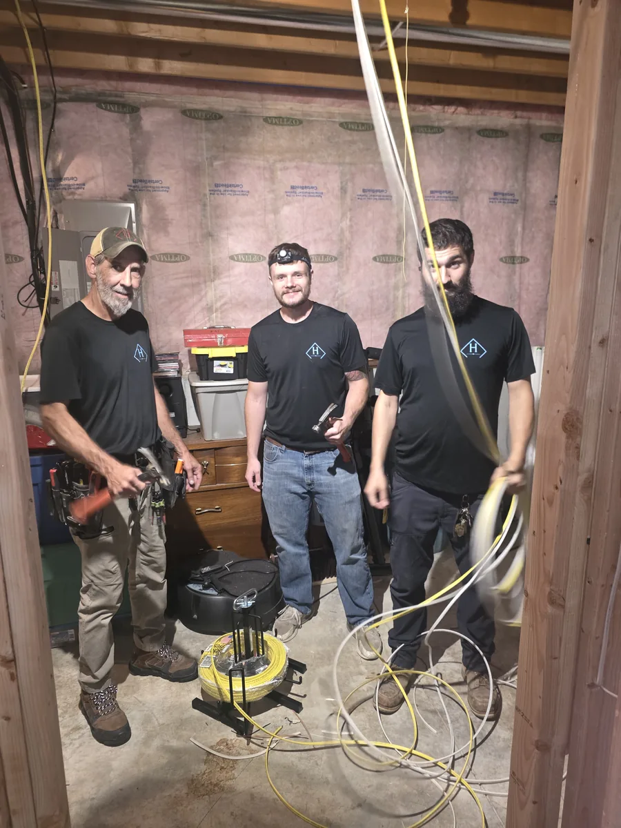 Electricians working overhead in an unfinished basement ceiling